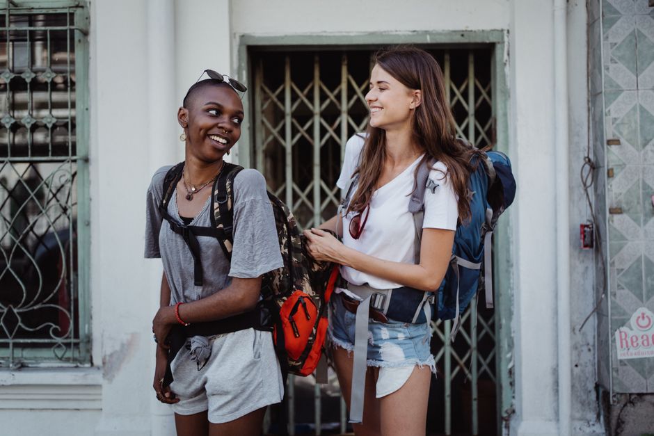 Two young women backpacking and smiling in a lively urban setting, ideal for travel-focused content.
